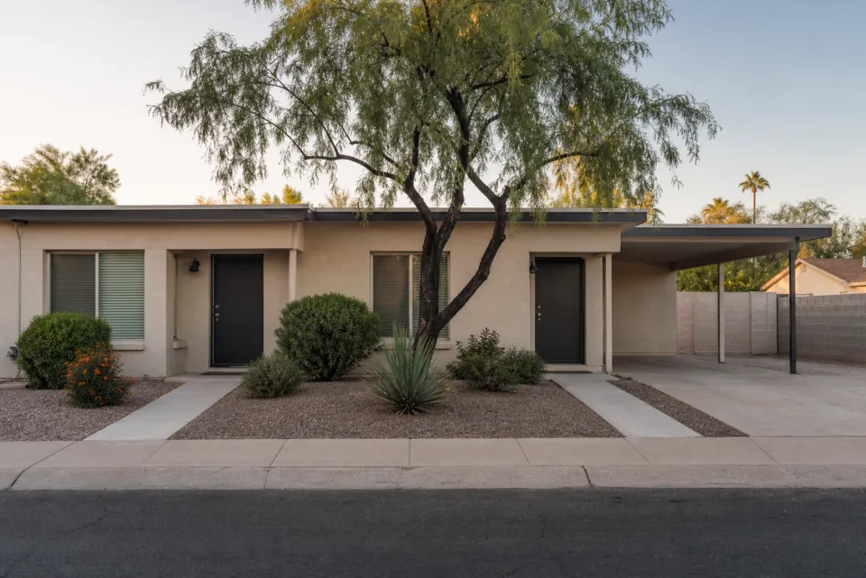 A modest two-unit Phoenix-area duplex with two entrances, desert landscaping, and covered parking.