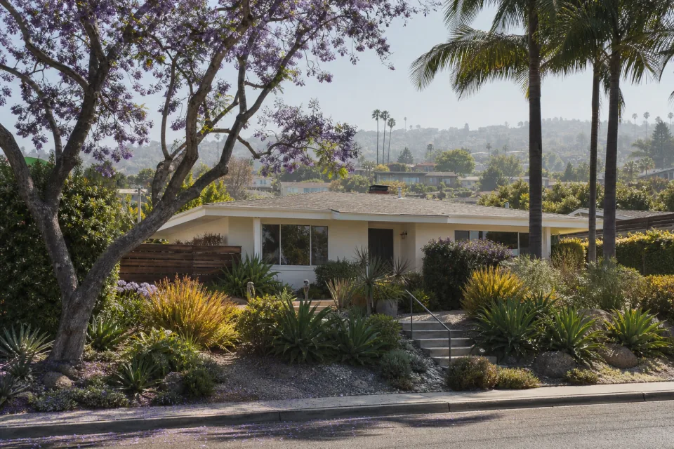 A well-kept mid-century Southern California bungalow on a green hillside street.